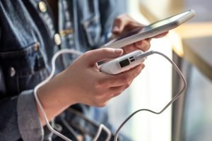 Seseorang memegang handphone dalam keadaan di charge dengan powerbank tanpa melepaskan case handphonenya.